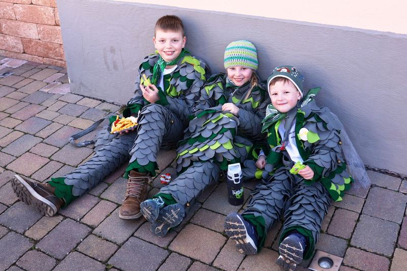 Drei Kinder im grünen Häs der Rhinschnooge machen Pause am Straßenrand